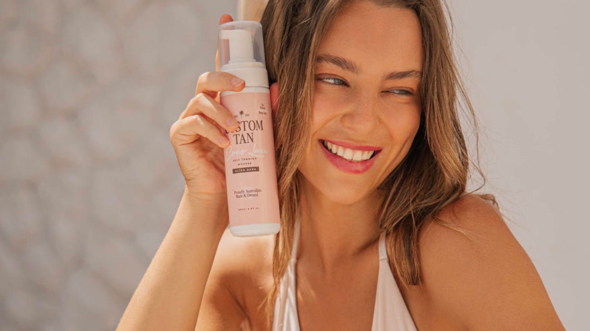 smiling woman holding a bottle of Custom Tan self tanning mousse
